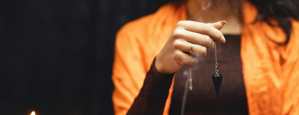 Main qui tient un pendule divinatoire sur un fond noir