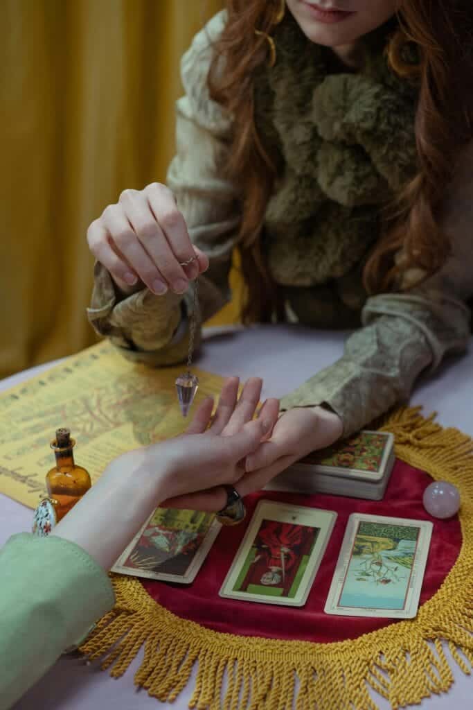 Femme qui fait une séance de pendule en tenant la main dune autre femme avec des cartes sur la table