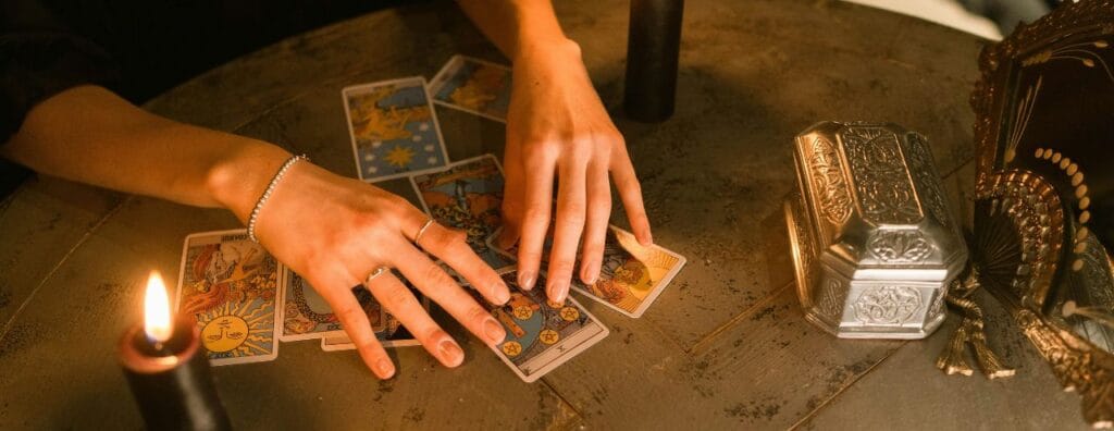 mains posées sur des cartes de tarot sur une table en bois avec une bougie posée à côté